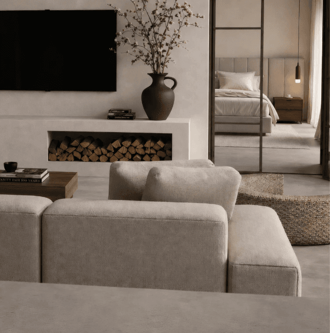 Living room with cream sofa, stacked firewood and a view through a loft door into a calm bedroom
